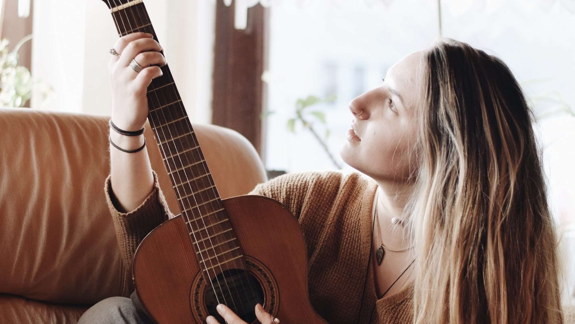 Woman playing classical guitar next to a window